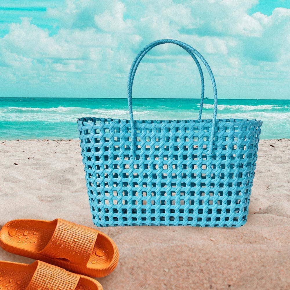Blue woven beach bag on a sandy beach with turquoise water and sky.