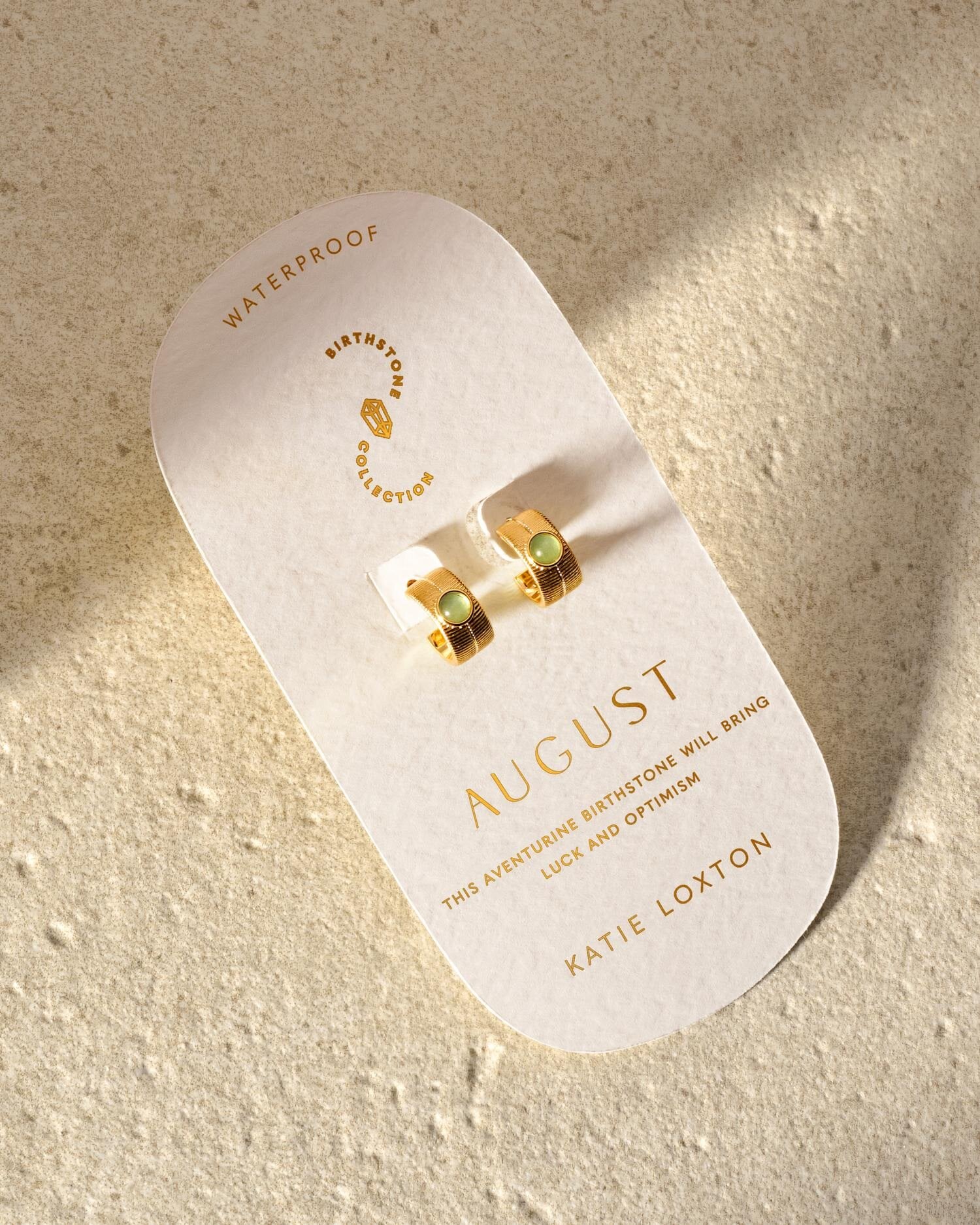 Gold hoop earrings with green aventurine stones on a Katie Loxton August birthstone display card