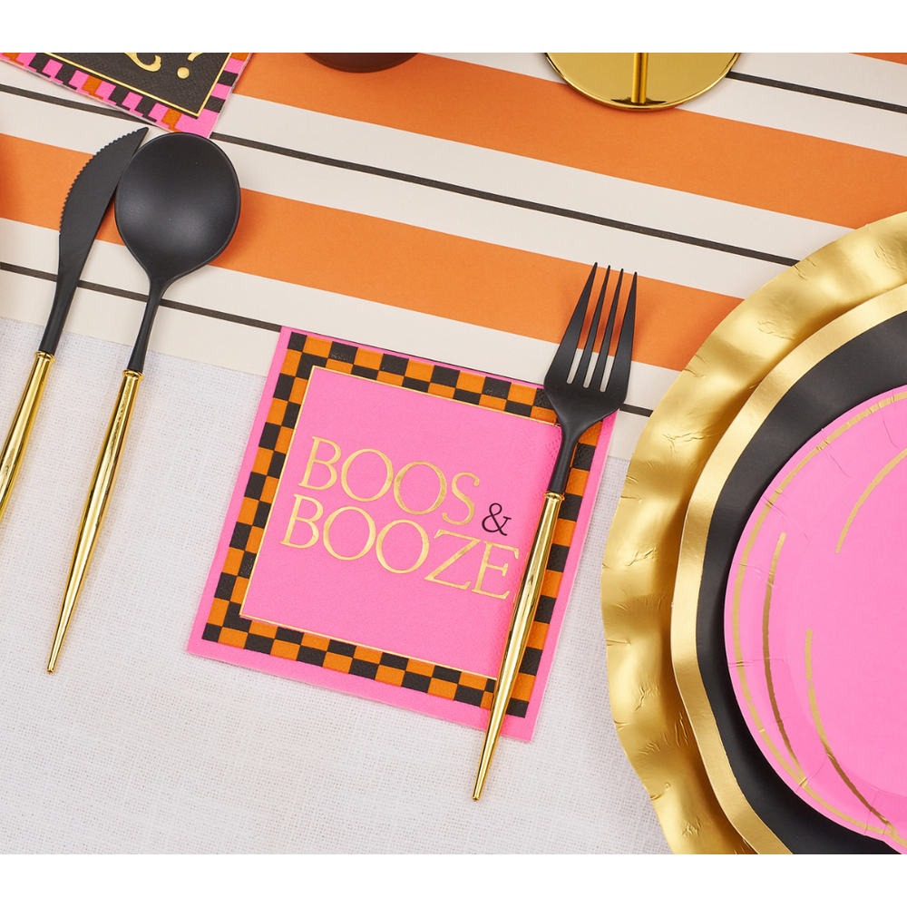 Pink paper napkin with black and orange checkered border and gold text reading Boos and Booze on a table setting
