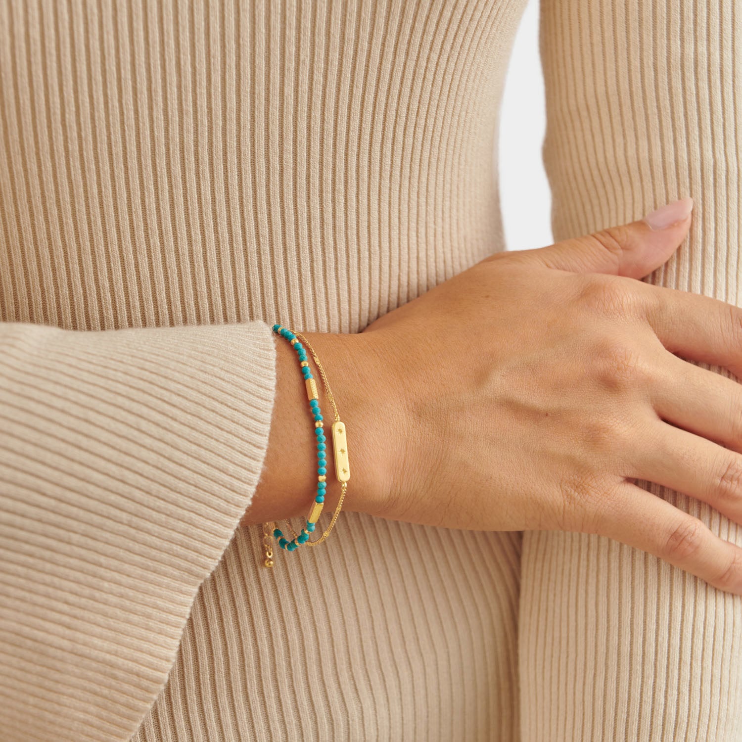 Two gold bracelets with turquoise beads and a rectangular charm worn on a wrist