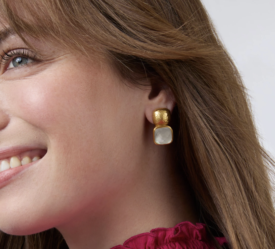 Woman wearing gold textured stud earrings with a square white stone drop