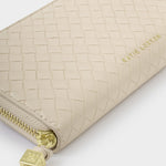 Product photography by Katie Loxton of a beige woven wallet on a plain white background featuring a gold-tone embossed logo and a metallic gold zipper with a square engraved charm