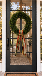 Black front door with a boxwood wreath and a copper and olive ribbon sash