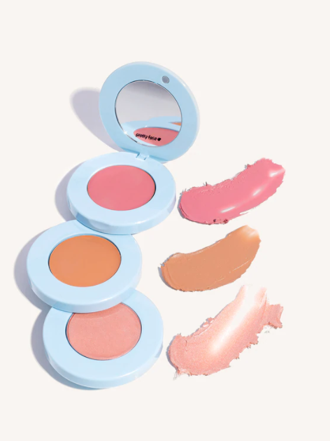 Three round cream blush compacts in light blue cases with matching product swatches