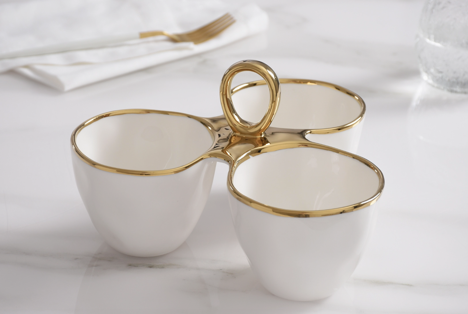 White ceramic three-compartment serving dish with elegant gold trim and a prominent central gold handle resting on a pristine white marble surface