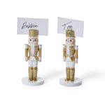Two white and gold nutcracker place card holders holding cards reading "Bobbie" and "Tom"