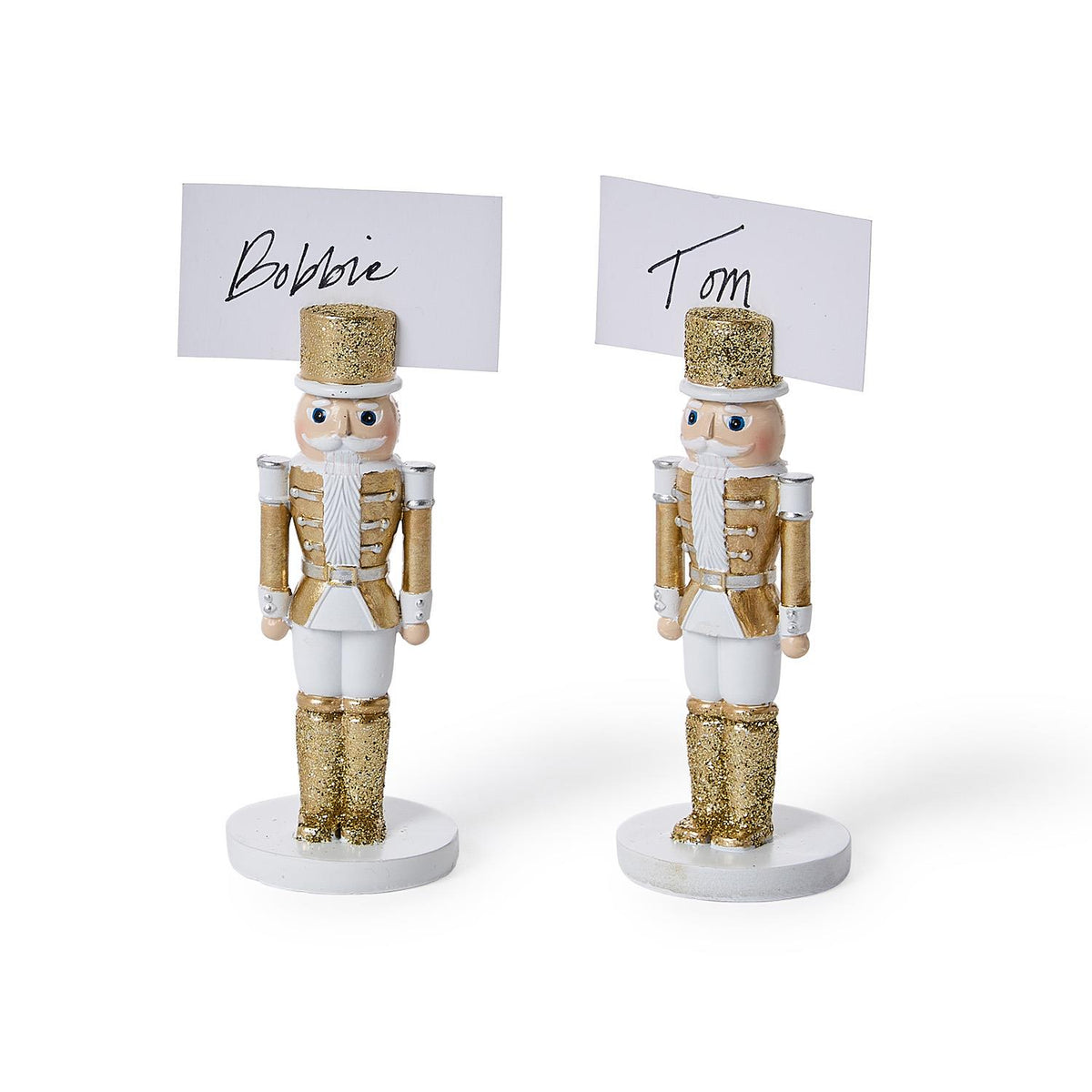 Two white and gold nutcracker place card holders holding cards reading "Bobbie" and "Tom"