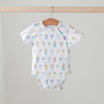 Baby onesie with colorful snoball pattern hanging on a wooden hanger against a light gray background