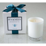 White candle in a glass jar next to a gift box with a teal ribbon and Bs Knees Fragrance Co label