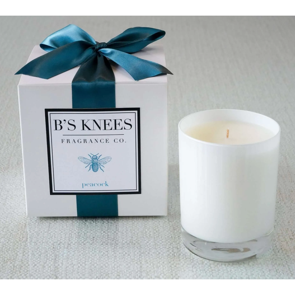 White candle in a glass jar next to a gift box with a teal ribbon and Bs Knees Fragrance Co label