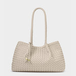 Handcrafted woven leather handbag featuring a cream Intrecciato pattern, a single long braided shoulder handle, and gold-toned cube charms on slender leather ties against a neutral studio background