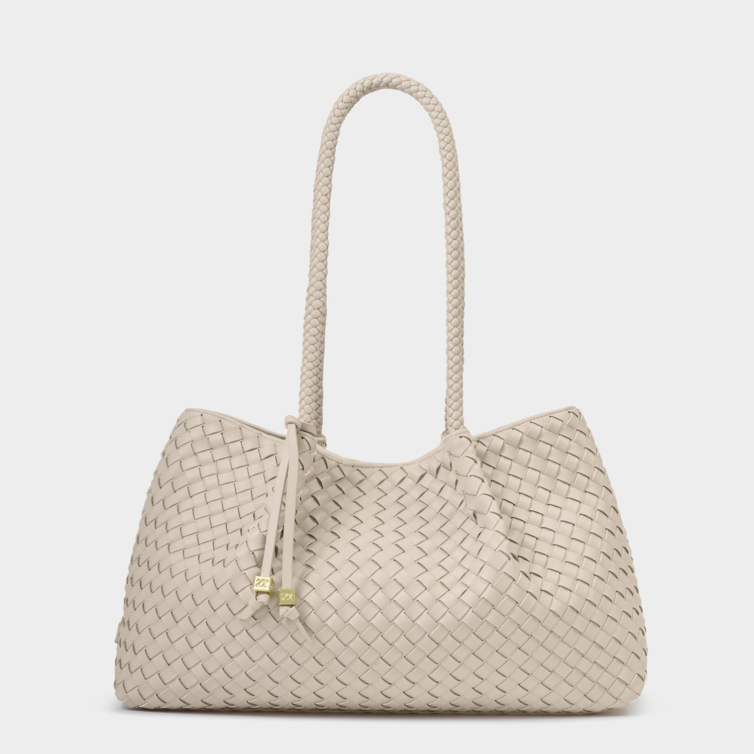 Handcrafted woven leather handbag featuring a cream Intrecciato pattern, a single long braided shoulder handle, and gold-toned cube charms on slender leather ties against a neutral studio background