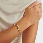 Gold chain and green beaded bracelet on a wrist