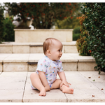 Baby sitting on stone steps outdoors with greenery in the background