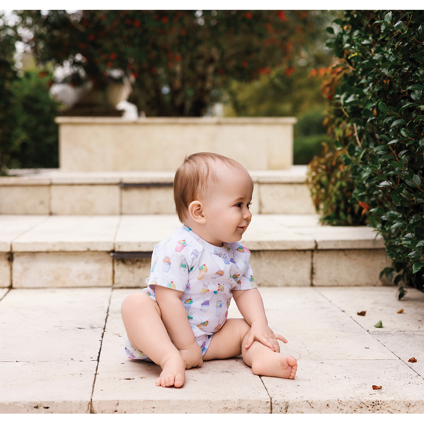 Baby sitting on stone steps outdoors with greenery in the background