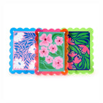 Acrylic art frames featuring scalloped translucent edges in blue, fuchsia, and lime green, each displaying a unique bold floral pattern with white daisies on pink, pink blossoms on teal, and magenta flowers on navy