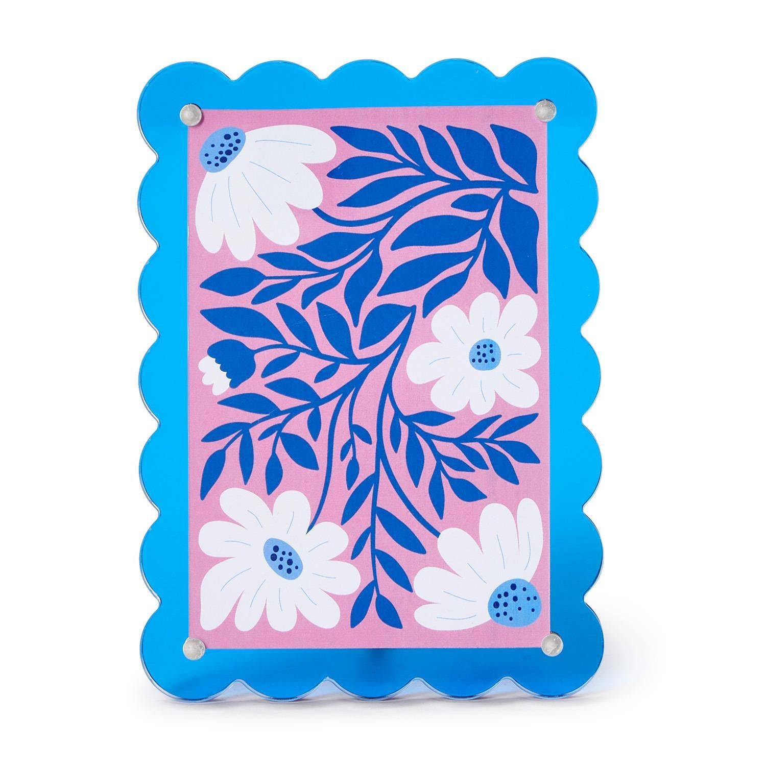 Decorative print featuring bold white and blue floral patterns on a pink background, housed in a vibrant scalloped blue acrylic frame with silver corner details