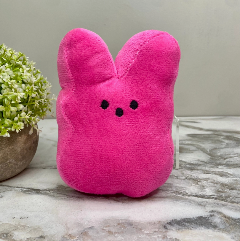 Plush toy hot pink Peeps bunny with black dot eyes and nose on a marble surface next to a small green potted plant