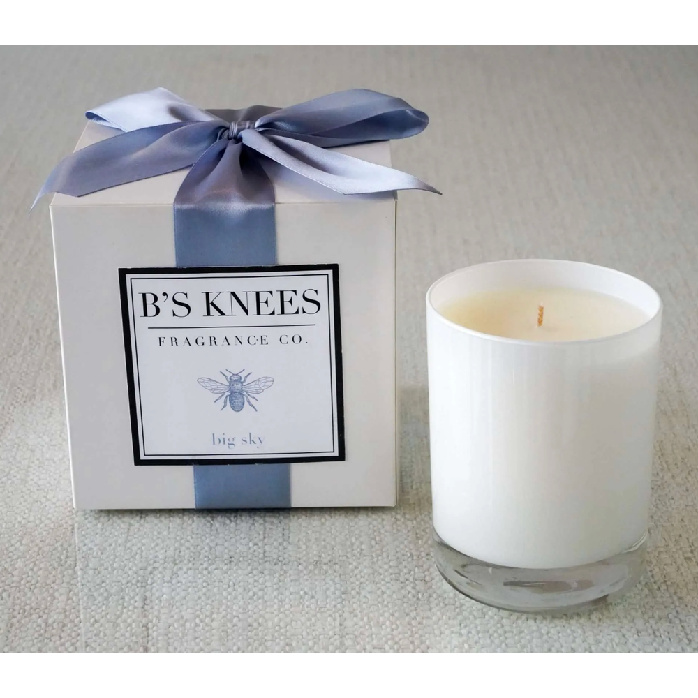 White candle in glass jar next to a white gift box with a blue ribbon and Bs Knees Fragrance Co label