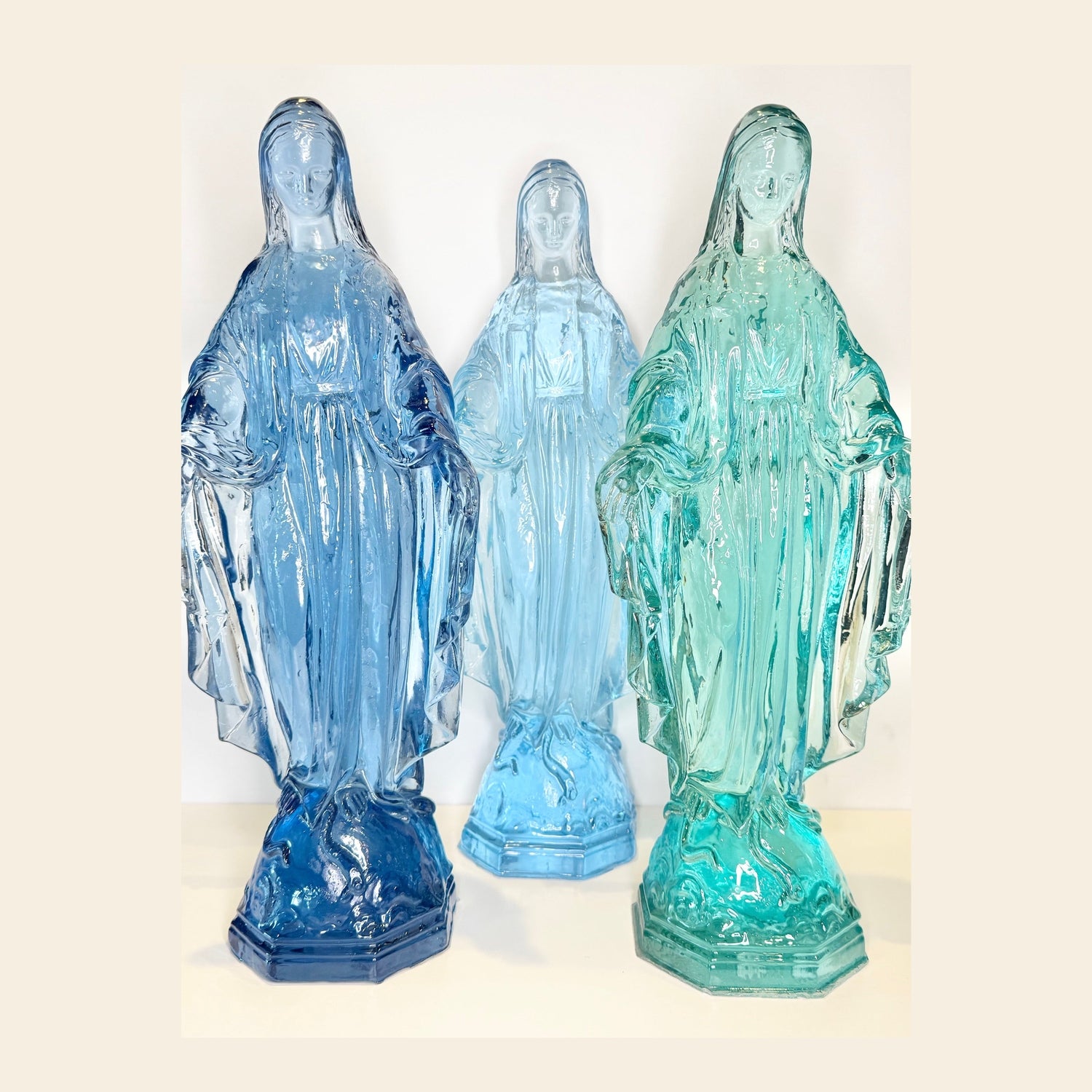 Three acrylic statues of a woman in blue, light blue, and green on a white background