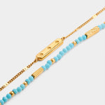 Two layered gold bracelets one with a star engraved bar and one with turquoise beads and gold accents