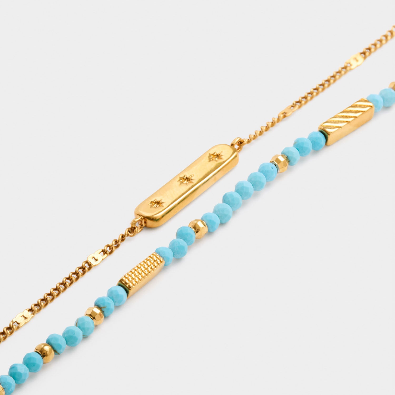 Two layered gold bracelets one with a star engraved bar and one with turquoise beads and gold accents
