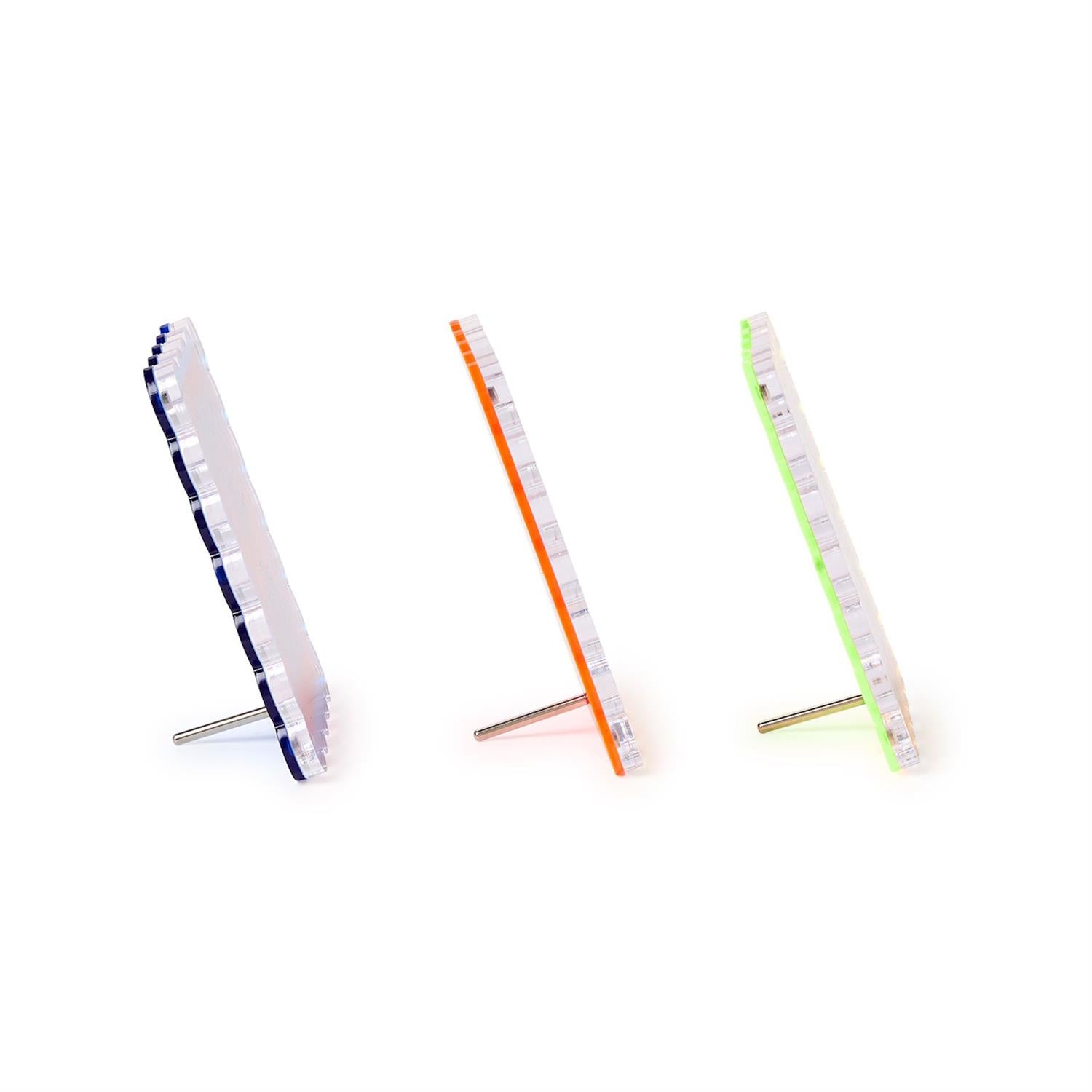 Three clear acrylic photo stands with prominent blue, orange, and neon green colored edges supported by silver metal pegs on a pure white background