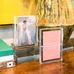 Acrylic frames displaying an art print of a figure and a pink card with an inspirational quote on a wooden surface