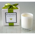 White candle in glass jar next to a white gift box with a green ribbon and Bs Knees Fragrance Co label