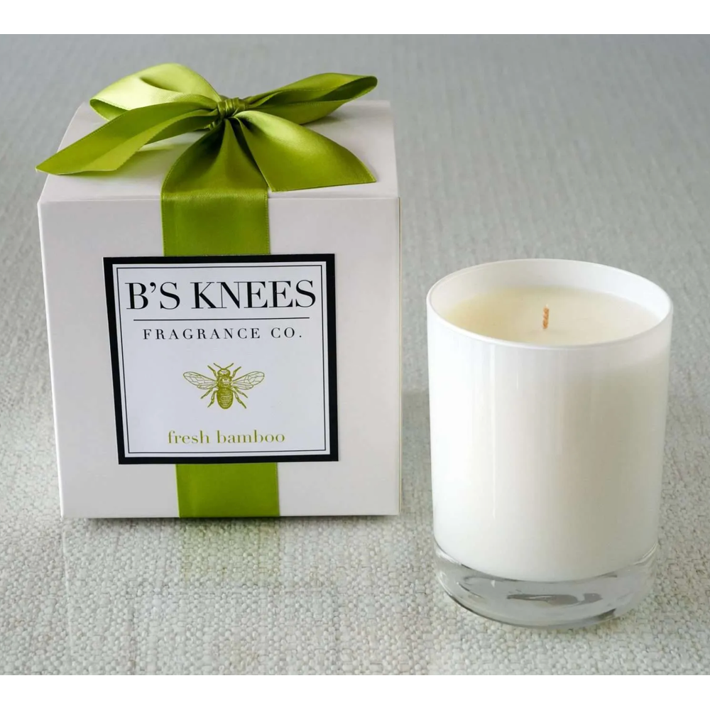 White candle in glass jar next to a white gift box with a green ribbon and Bs Knees Fragrance Co label