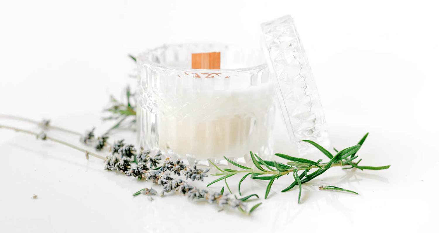 Candle in a cut glass jar with lavender sprigs and rosemary on a white surface