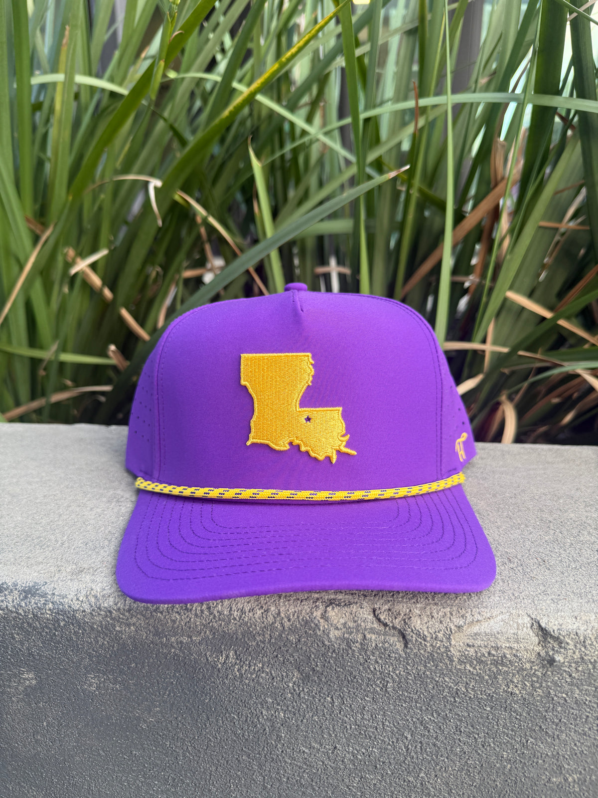Purple Baton Rouge rope hat with a gold Louisiana patch on a stone ledge