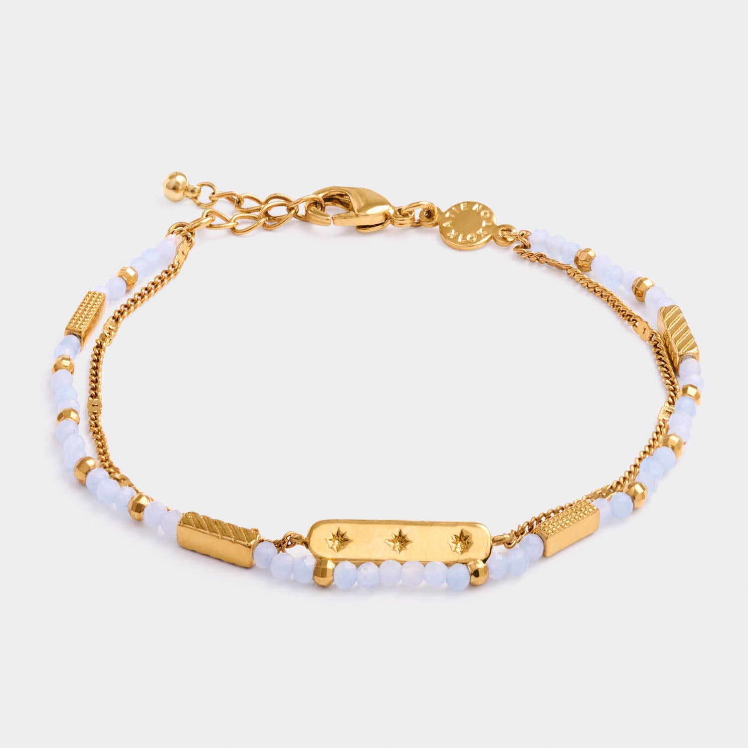 Gold chain bracelet with light blue beads and a central rectangular charm featuring three star engravings