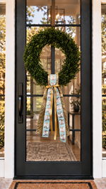 Black front door with a boxwood wreath and a gold and aqua pumpkin ribbon sash