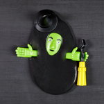 Green witch face and hands emerging from a black puddle holding a yellow broom
