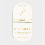 Two gold bracelets with turquoise beads on a December birthstone collection display card