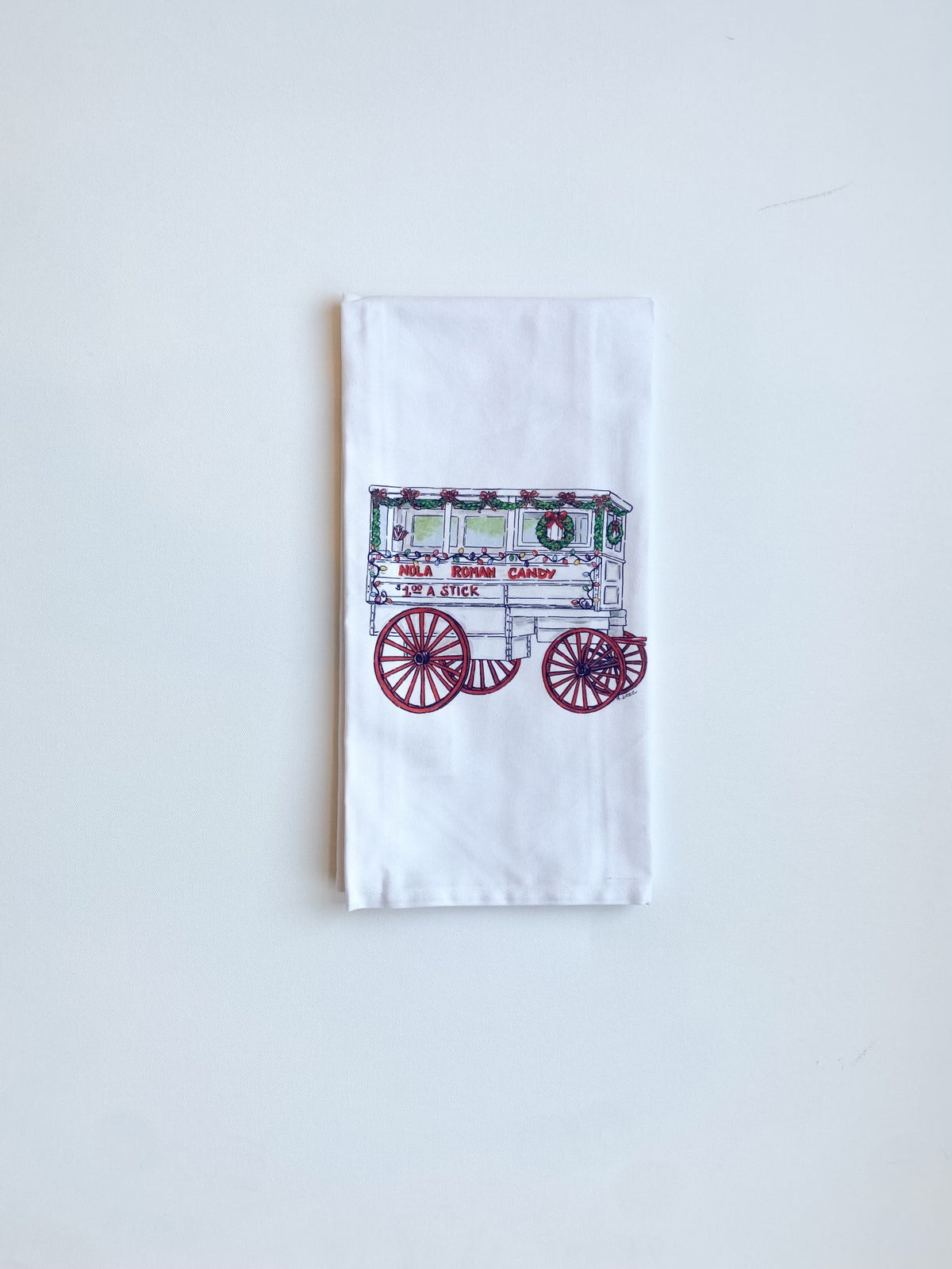 White towel printed with a candy cart decorated with a Christmas wreath, reading "NOLA Roman Candy"