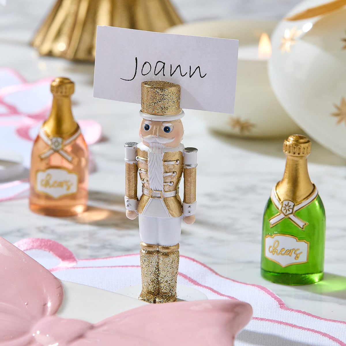 White and gold nutcracker place card holder holding a card reading "Joann" on a holiday table