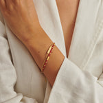 Gold chain bracelet with a small rectangular charm and a second strand of red beaded gemstones on a wrist