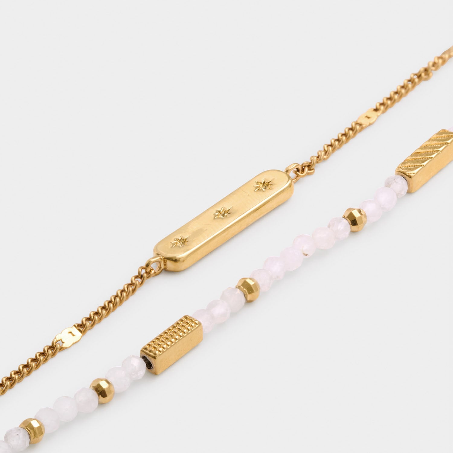 Two layered gold bracelets one with star engraved bar and one with pink beaded stones and gold accents