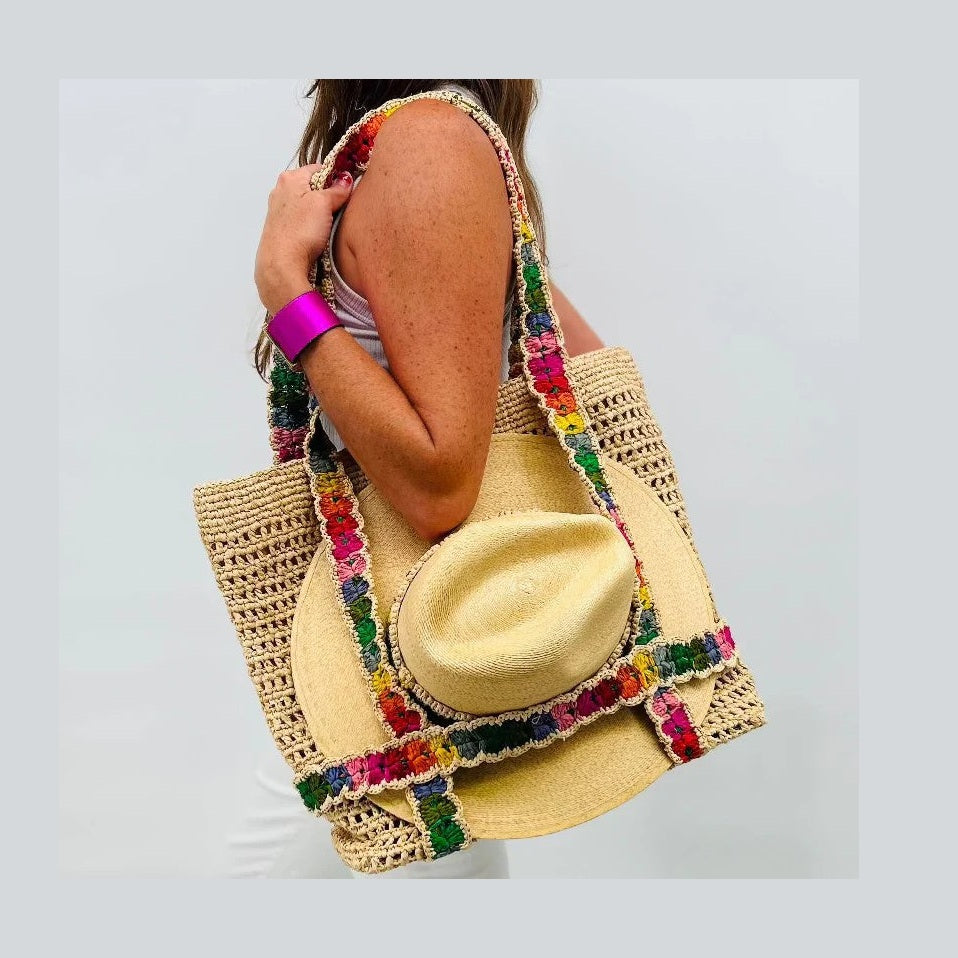 Person holding a colorful crochet bag with a yellow straw hat against a light gray background