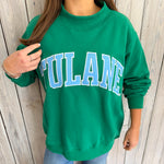 Green sweatshirt with 'TULANE' text worn by a person against a wooden background