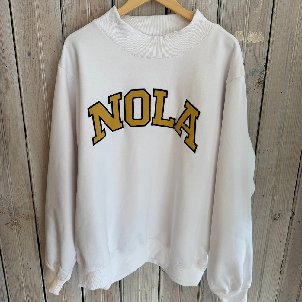White crewneck sweatshirt with NOLA text in gold and black lettering