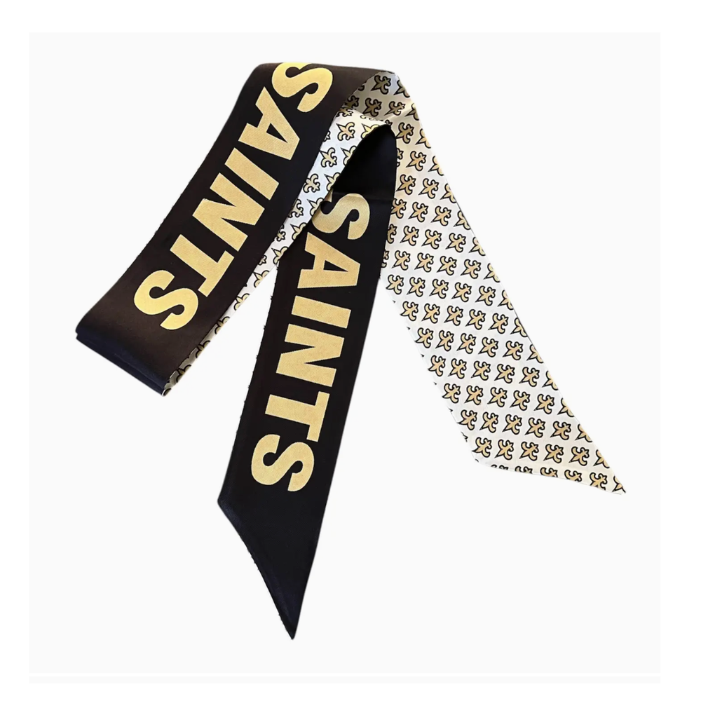 Silk twilly scarf featuring the New Orleans Saints brand in bold gold block lettering and a repeating fleur-de-lis pattern on the white reverse side with pointed ends