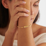 Gold chain bracelet with a small rectangular charm featuring star engravings worn on a wrist