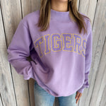 Person wearing a purple 'TIGERS' sweatshirt against a wooden background