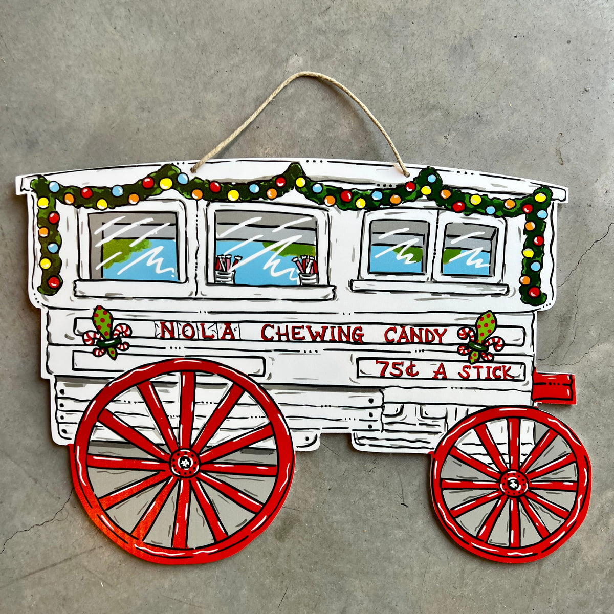 Door hanger of a white candy cart with red wheels and Christmas garland, reading "NOLA Chewing Candy 75¢ a stick"