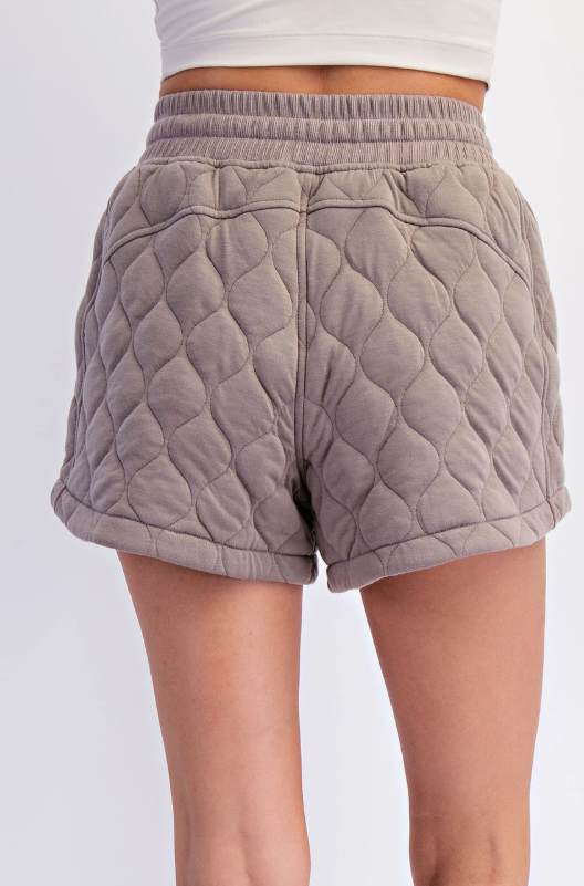 Rear view of a person modeling taupe quilted shorts featuring a distinct wavy pattern and a ribbed elastic waistband against a clean white background