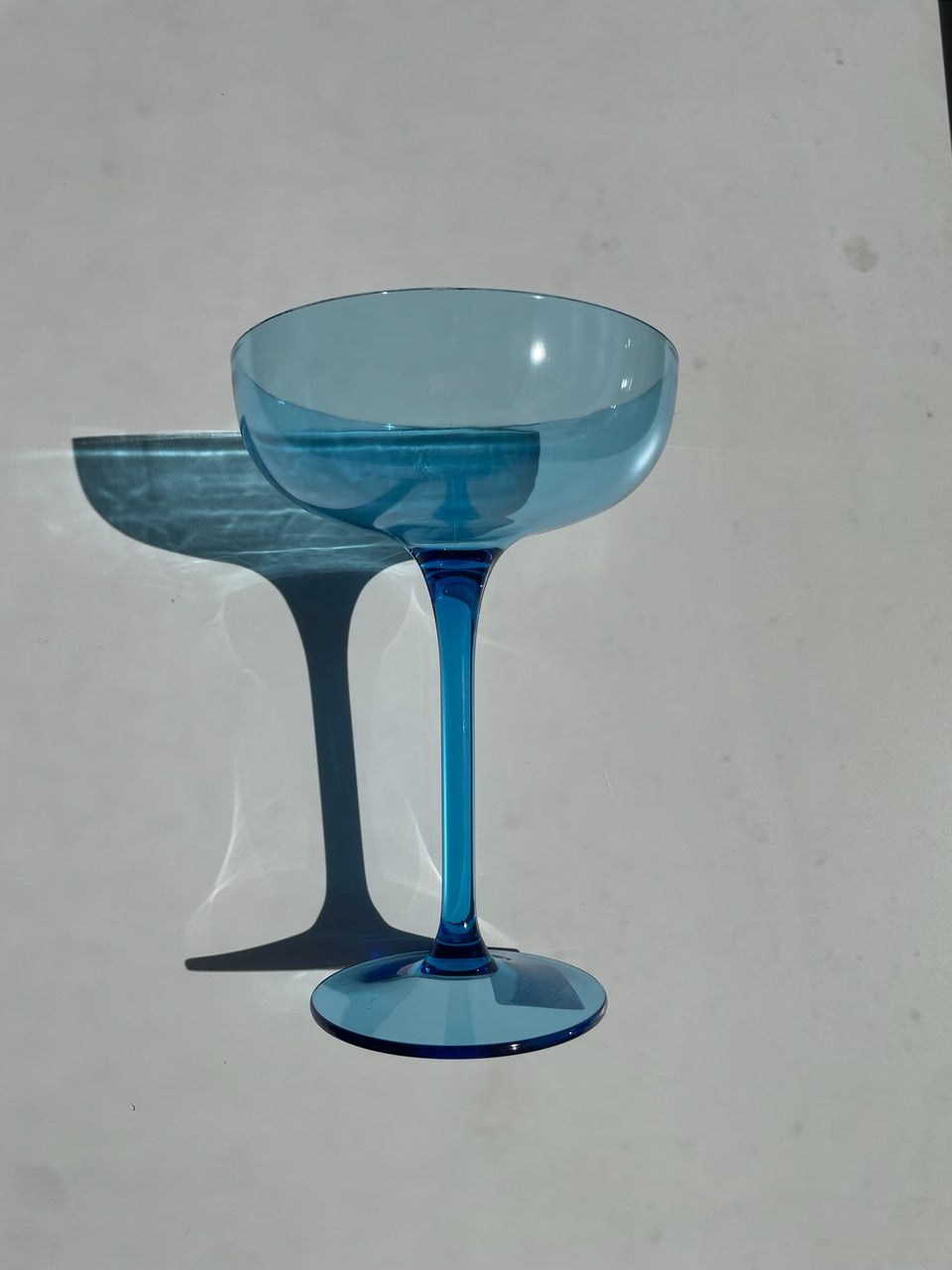 A vibrant blue glass coupe stands on a bright white surface casting a dramatic shadow and light reflections