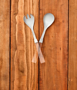 Stainless steel salad servers with clear acrylic handles crossed on a wooden surface